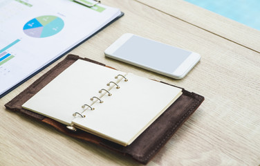 Open blank organizer book with mobile phone and business chart on wood table at office.