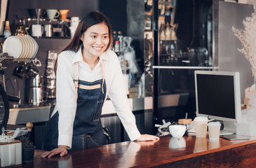 Asian female barista wear jean apron place her hand on counter bar and smiling to customer,cafe...