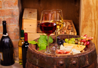 Red and white wine with cheese, prosciutto and grape on old wine barrel in cellar. Food and drinks...