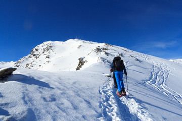 Fototapeta na wymiar Group of people hiking on snowshoes and mountain snow panorama with summit cross in Stubai Alps, Austria