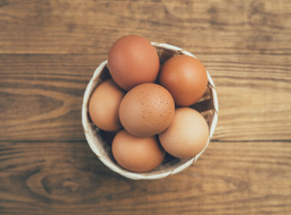 Fresh eggs in white basket on wooden background