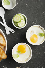 Breakfast for two. Eggs baked in the oven in ceramic portioned forms with toasted bread and slices of fresh cucumber. Top View.