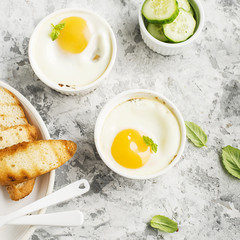 Breakfast for two. Eggs baked in the oven in ceramic portioned forms with toasted bread and slices of fresh cucumber. Top View.