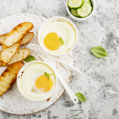 Breakfast for two. Eggs baked in the oven in ceramic portioned forms with toasted bread and slices of fresh cucumber. Top View.