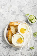 Breakfast for two. Eggs baked in the oven in ceramic portioned forms with toasted bread and slices of fresh cucumber. Top View.