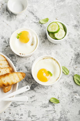 Breakfast for two. Eggs baked in the oven in ceramic portioned forms with toasted bread and slices of fresh cucumber. Top View.