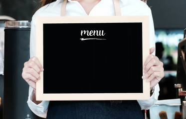 Woman holding blank menu blackboard at cafe background, copy space for text