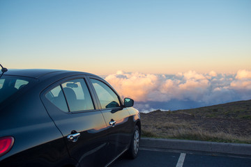 Fototapeta na wymiar Black car in mountains above the clouds at sunset or sunrise