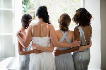 Rear view of bride and bridesmaids standing together near window - obrazy, fototapety, plakaty