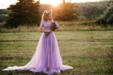 beauty woman portrait with wreath of flowers on head at sunset. bride in purple dress Outdoor. soft focus