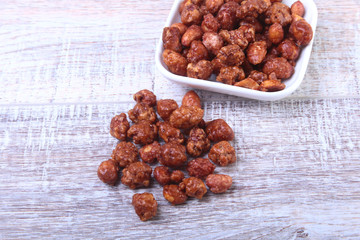 Sugared Hazelnuts in a white bowl on a wooden background. Hazelnuts in sugar glaze. Selective focus.