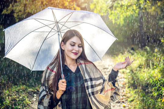 Happy young woman walking in a Sunny Park with a white umbrella in the rain. Concept of seasons and autumn mood