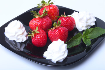 Fresh strawberries with whipped cream and mint leaves on a black plate. Selective focus.