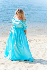 Nice woman in blue long dress walk on a beach and relax at warm day. Tenderness plus size blonde hair lady look stylish and sweet