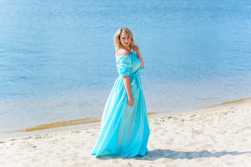 Fototapeta na wymiar Nice woman in blue long dress walk on a beach and relax at warm day. Tenderness plus size blonde hair lady look stylish and sweet