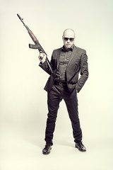 Bald man in a gray suit and sunglasses standing with arms raised up. Toned