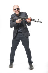 Smiling bald man in a gray suit and sunglasses standing with a gun in his hand. Isolated