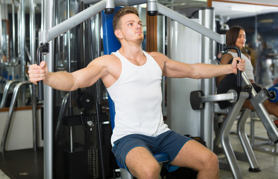 strong young man training upper body using fly machine