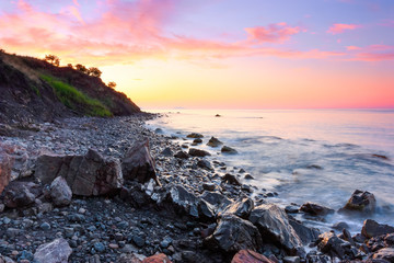 On the shore of the sea covered with stones opens a view on a beautiful landscape of a sunset.