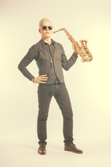 Elegant blond man dressed in black holding a saxophone. Toned