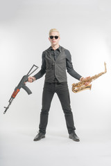 Elegant blond man in sunglasses dressed in black holding a saxophone in one hand and in the other...