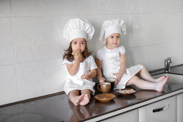 two little baker girls are drinking tea with a pabcakes in the kitchen