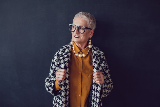 Stylish old woman in glasses standing on a black background.