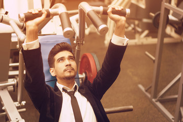 Handsome young man in a black suit, white shirt and tie training in the gym