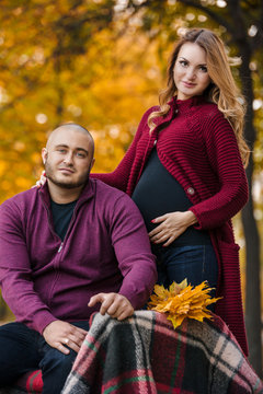 Pregnant woman and her husband in the yellow maple park in leaves
