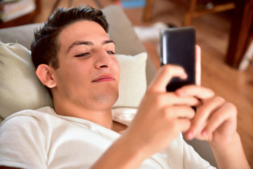 Young boy face up on couch playing with a smartphone