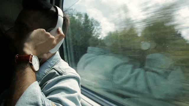 Ragazzo sta viaggiando su un treno mentre ascolta musica dalle cuffie e usa lo smart phone.