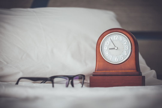 Glasses and alarm clock on the white bed
