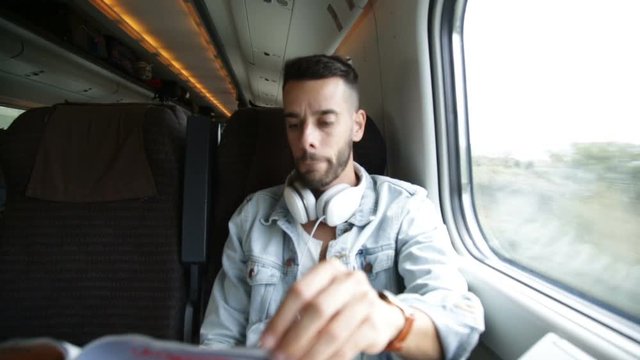 Ragazzo sta viaggiando su un treno mentre ascolta musica dalle cuffie e usa lo smart phone.