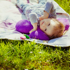 Happy little girl lies on white blanket on the lawn