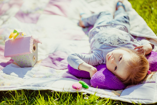 Happy little girl lies on white blanket on the lawn