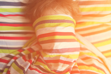 Sleepy girl teenager covered her face under a colored striped blanket, sunny. Toned