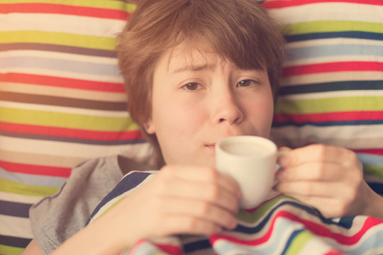 Cute teenager girl lying in bed with a cup of coffee in hand. Toned
