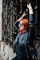 Naklejka premium Red haired stylish girl in sunglasses wear in black, against abadoned place.