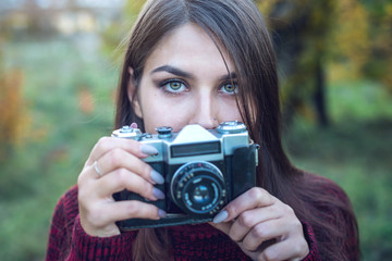 Beautiful woman in autumn Park holds vintage retro camera. Concept of photography as a hobby