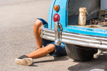 The legs of a man under the car, Vinales, Pinar del Rio, Cuba. Car repairs. Close-up.