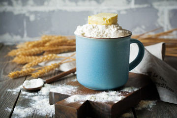 Ingredients and tools for homemade baking, flour and butter in a ceramic cup on an old wooden background. Selective focus.