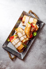 Fresh baguette sandwich bahn-mi styled. Bacon, roasted cheese, tomatoes and lettuce on metallic background. Top view, copy space.