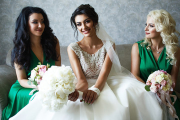 Bride and bridesmaids in green dresses sit on grey sofa in the room