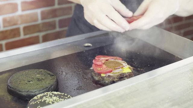 Hands of chef putting tomatos on a grilled burger