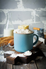 Ingredients and tools for homemade baking, flour and butter in a ceramic cup on an old wooden background. Selective focus.