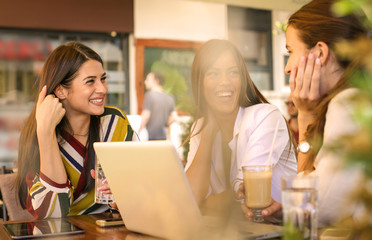 Three young women having conversation in cafe and using laptop.