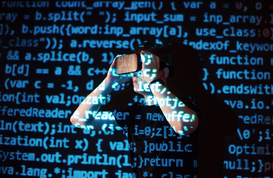 Double exposure of a caucasian man and Virtual reality headset is presumably a gamer or a hacker cracking the code into a secure network or server, with lines of code