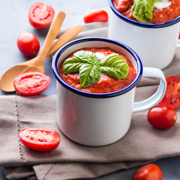 Creamy Tomato soup in enamel mugs on blue background