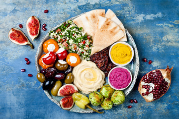 Meze-Platte aus dem Nahen Osten mit grüner Falafel, Pita, sonnengetrockneten Tomaten, Kürbis- und Rüben-Hummus, Oliven, gefüllter Paprika, Taboulé, Feigen. Idee für eine mediterrane Vorspeisenparty