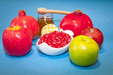 Jewish symbols, the Jewish New Year Rosh Hashanah concept - apple shaped plate with red pomegranate seeds on a blue background with honey. Rosh Hashanah greeting.
